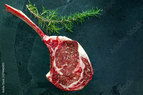 Raw, dry-aged wagyu tomahawk steak and rosemary on a  black stone table. Top view and copy space