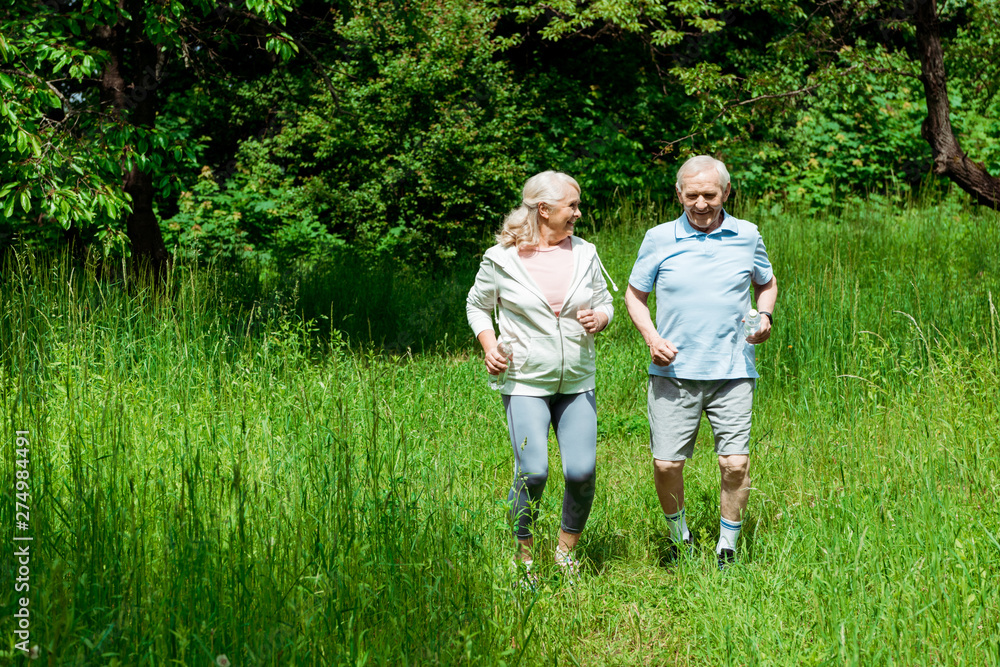 Fototapeta premium senior woman with grey hair looking at husband while running in park