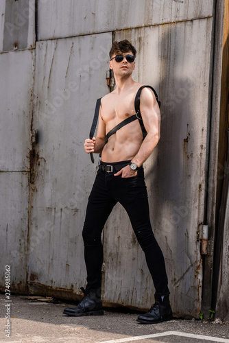 full length view of sexy shirtless man in black sunglasses and sword belt with hand in pocket