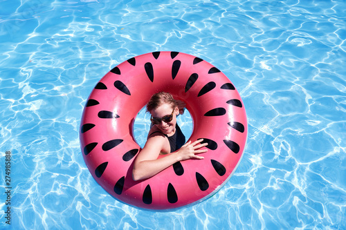 Portrait of woman with short hair swimming in a pool  look laughing through pink floatie Inflatable doughnut  blue water. Funny mood.