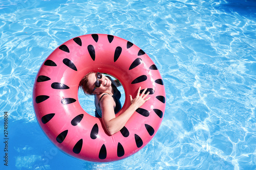 Woman with short hair swimming in a pool  look laughing through pink floatie Inflatable doughnut  blue water. Funny mood. Space for text layout.