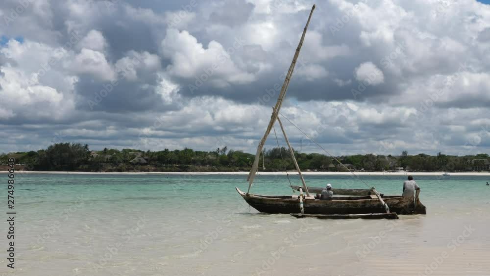 Static, shot of a people sitting in their sailboat, in turquoise water, at a white sand beach, in Mombasa, on a sunny day, in Kenya, Africa Static, shot of a people sitting in their sailboat, in turquoise water, at a white sand beach, in Mombasa, on a sunny day, in Kenya, Africa