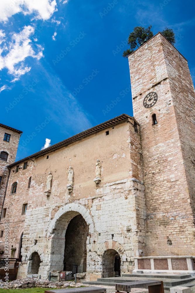 The Roman consular door, with the tower and the clock. One of the accesses to the city walls. Three statues above the arch. In Spello, province of Perugia, Umbria, Italy.