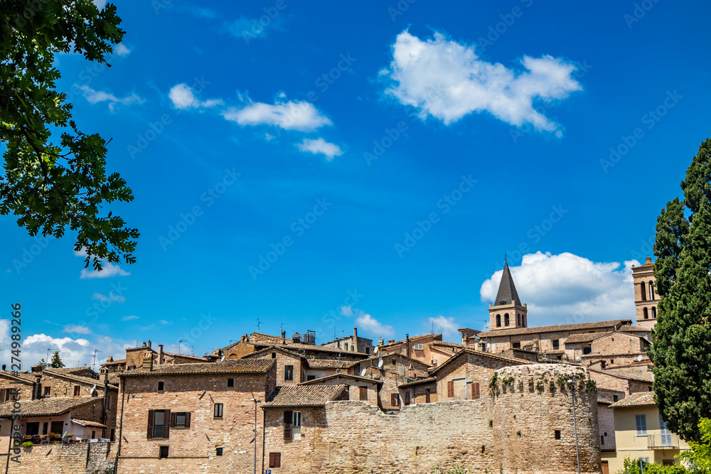 A view of the medieval village of Spello, with stone and brick houses, city walls. The blue sky in the summer. In the province of Perugia, Umbria, Italy.