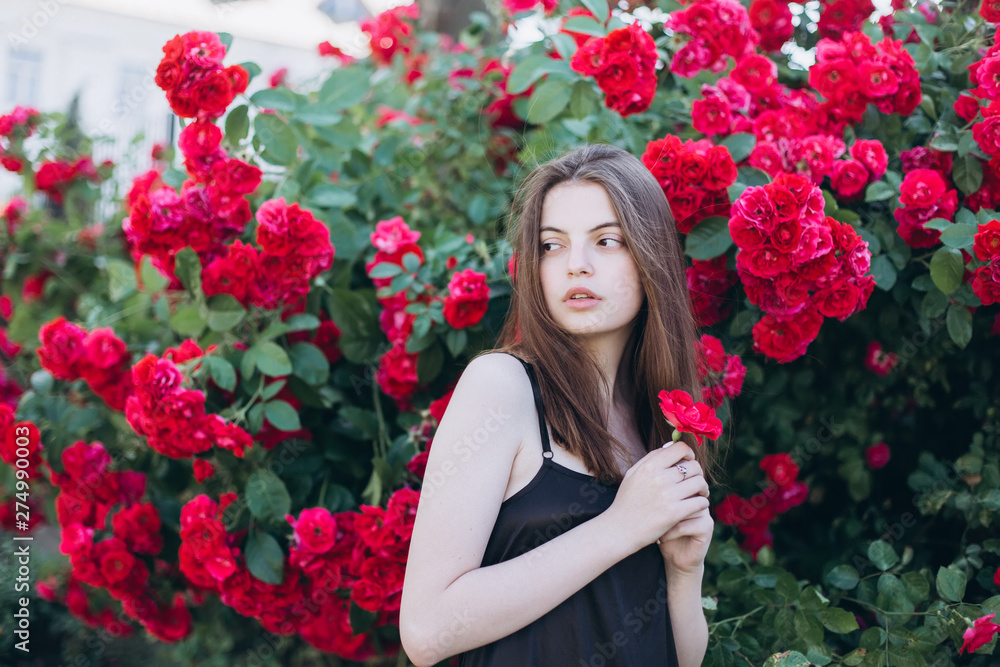 Close up summer portrait of young sensual interesting pretty young woman outdoors near red roses. Modeling, fashion, trendy, nature concept
