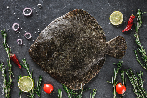 Fototapet Raw whole flounder fish with rosemary, onions and spices on dark stone background