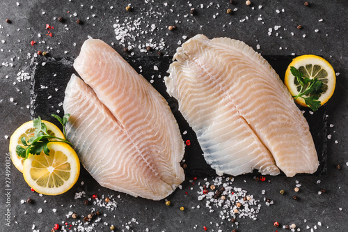 Photo Fresh raw fillet white fish Pangasius with spices and lemon on dark stone background