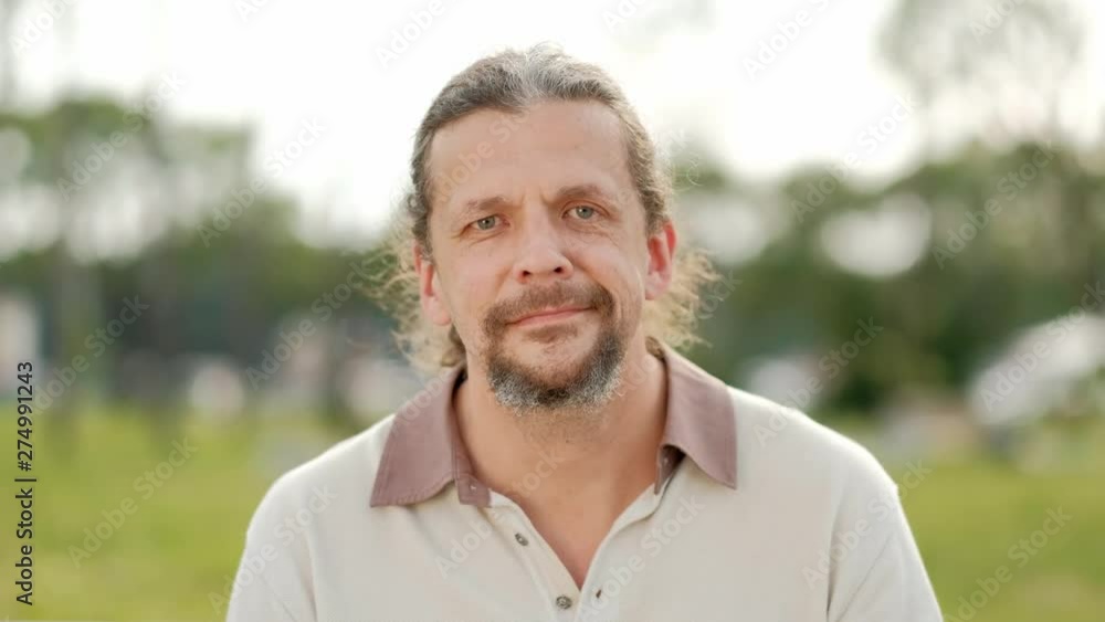 A relaxed attractive middle aged man with long gray hair looks into the camera, smiles and laughs. Close-up face. A relaxed attractive middle aged man with long gray hair looks into the camera, smiles and laughs. Close-up face.