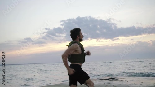 Young bearded athlete training outdoor with weighted vest, exercise with military plate carrier