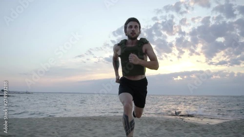 Young bearded athlete training outdoor with weighted vest, exercise with military plate carrier