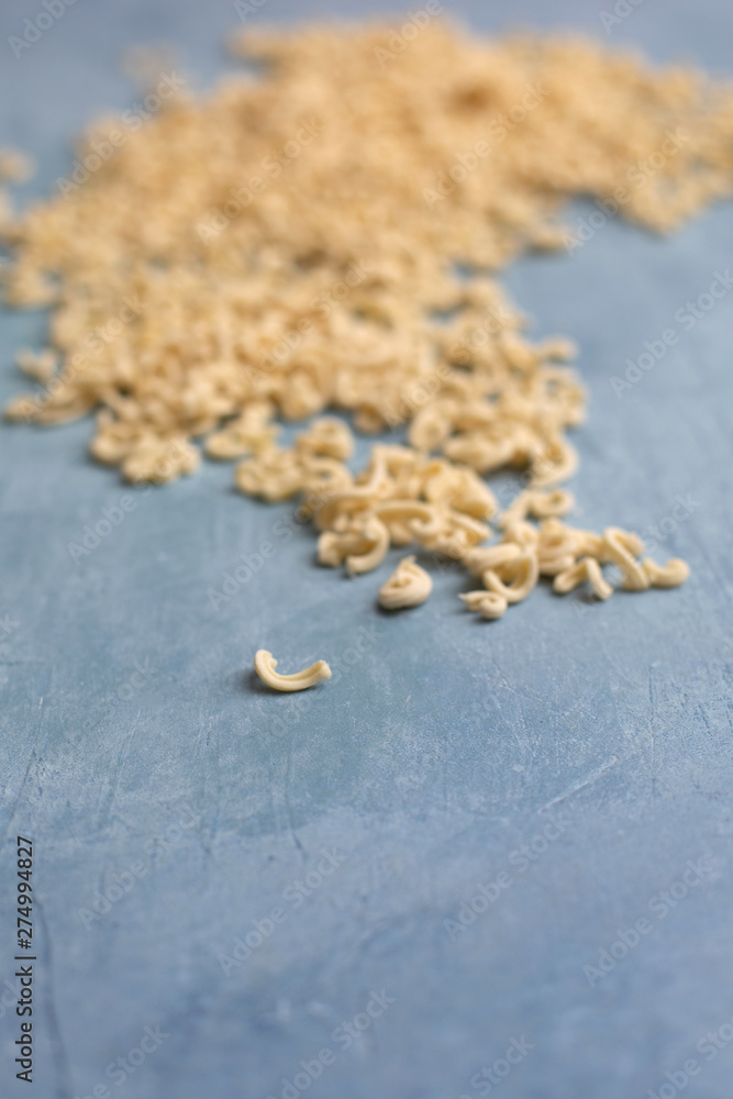 Homemade Small Macaroni Pasta Scattered on Blue Background Homemade Small Macaroni Pasta Scattered on Blue Background