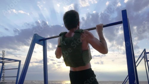 Young bearded athlete training outdoor with weighted vest, exercise with military plate carrier