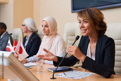 Happy young female delegate in formalwear looking at audience photo