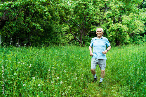 happy senior man with grey hair running in green park