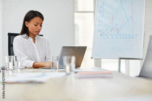 Portrait of young mixed race businesswoman using laptop while working in office, copy space