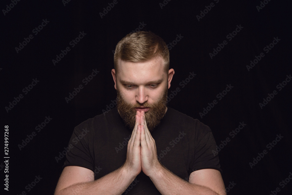 Close up portrait of young man isolated on black studio background. Photoshot of real emotions of male model. Praying looking down, looks hopeful. Facial expression, human emotions concept. Close up portrait of young man isolated on black studio background. Photoshot of real emotions of male model. Praying looking down, looks hopeful. Facial expression, human emotions concept.