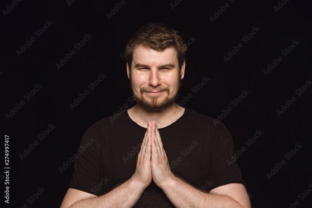 Close up portrait of young man isolated on black studio background. Photoshot of real emotions of male model. Praying and crying, looks sad and hopeful. Facial expression, human emotions concept. Close up portrait of young man isolated on black studio background. Photoshot of real emotions of male model. Praying and crying, looks sad and hopeful. Facial expression, human emotions concept.