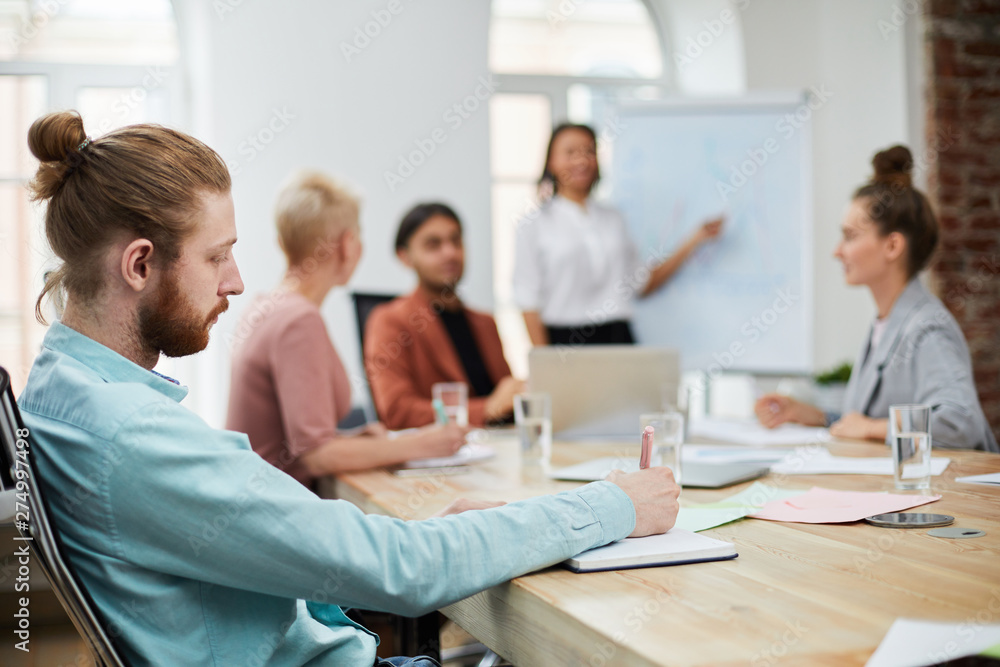 Side view portrait of bearded young man taking notes during business meeting in conference room, copy space Side view portrait of bearded young man taking notes during business meeting in conference room, copy space