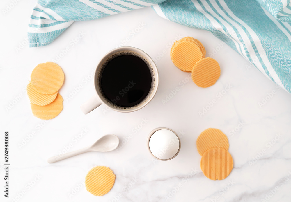 Top view of boiled egg in ceramic egg cup, cup of coffee and thin crispy corn chips on background of beautiful white peony. Breakfast concept. Copy space. Top view of boiled egg in ceramic egg cup, cup of coffee and thin crispy corn chips on background of beautiful white peony. Breakfast concept. Copy space.