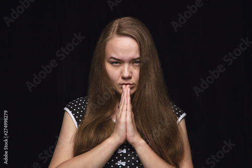 Close up portrait of young woman isolated on black studio background. Photoshot of real emotions of female model. Praying looking forward, sad and hopeful. Facial expression, human emotions concept.