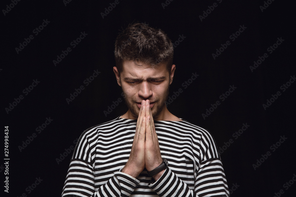 Close up portrait of young man isolated on black studio background. Photoshot of real emotions of male model. Praying and crying, looks sad and hopeful. Facial expression, human emotions concept. Close up portrait of young man isolated on black studio background. Photoshot of real emotions of male model. Praying and crying, looks sad and hopeful. Facial expression, human emotions concept.