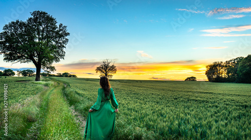 Portrait of a beautiful young woman in green dress on meadow watching the sunset enjoying nature