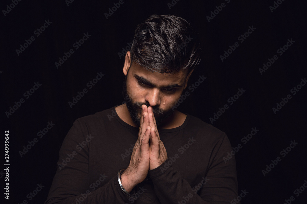 Close up portrait of young man isolated on black studio background. Photoshot of real emotions of male model. Praying and crying, looks sad and hopeful. Facial expression, human emotions concept. Close up portrait of young man isolated on black studio background. Photoshot of real emotions of male model. Praying and crying, looks sad and hopeful. Facial expression, human emotions concept.