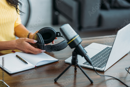 cropped view of radio host holding headphones while sitting near microphone