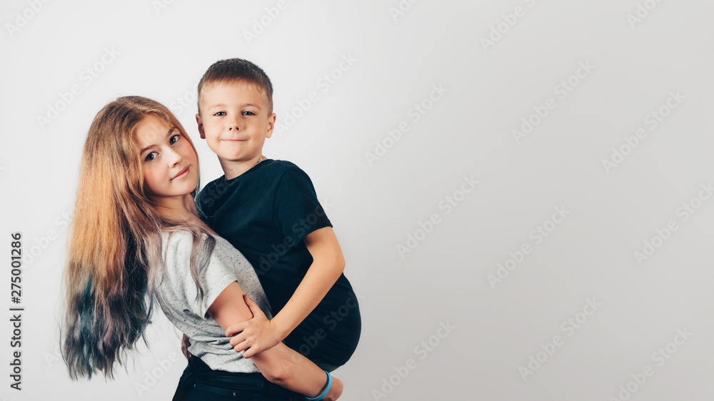 Happy family concept, sister and her little brother. Caucasian teen girl holding in her hands little boy. Gray wall on background. Copy space. 16:9 Happy family concept, sister and her little brother. Caucasian teen girl holding in her hands little boy. Gray wall on background. Copy space. 16:9