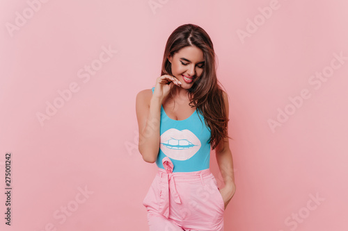 Tanned spectacular girl in funny tank-top posing on pink background. Indoor photo of brunette wonderful lady expressing positive emotions.