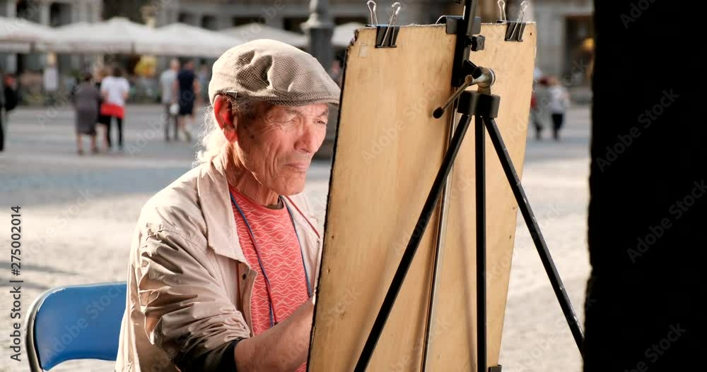 Skilled mature man painting in a public square in Madrid, Spain. Creative Spanish artist drawing with pencil on the street. People and creativity Skilled mature man painting in a public square in Madrid, Spain. Creative Spanish artist drawing with pencil on the street. People and creativity