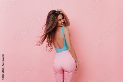 Portrait from back of laughing lovely lady in pink pants. Brown-haired girl in good mood posing in studio.