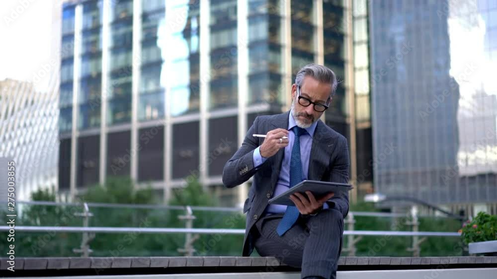 Thoughtful businessman working on financial report planning strategy for startup sitting on urban setting, pensive male expert in eyewear writing publication information by stylus pen Thoughtful businessman working on financial report planning strategy for startup sitting on urban setting, pensive male expert in eyewear writing publication information by stylus pen