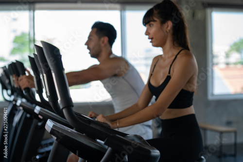 Defocused blurred medium shot of active man and woman smiling while doing aerobic cardio workout on training exercise bike at the fitness gym. Healthy weight loss fit and firm concept.