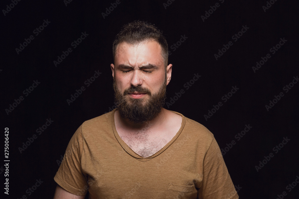 Close up portrait of young man isolated on black studio background. Photoshot of real emotions of male model. Crying with closed eyes, sad and hopeless. Facial expression, human emotions concept.