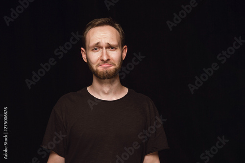 Close up portrait of young man isolated on black studio background. Photoshot of real emotions of male model. Crying, sad, dreary and hopeless. Facial expression, human emotions concept.