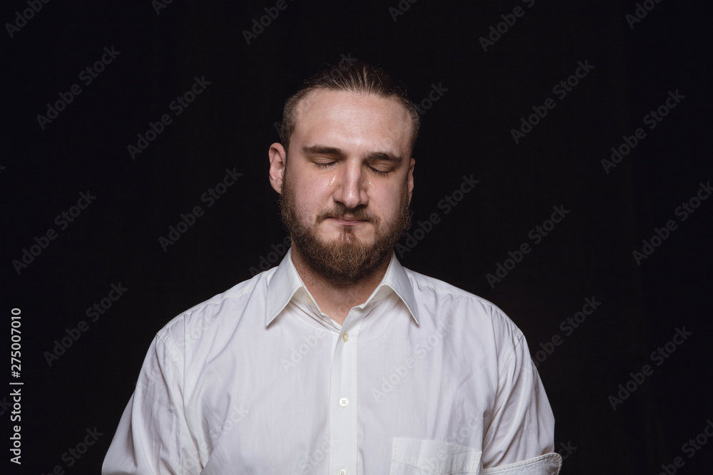 Close up portrait of young man isolated on black studio background. Photoshot of real emotions of male model. Crying with closed eyes, sad and hopeless. Facial expression, human emotions concept. Close up portrait of young man isolated on black studio background. Photoshot of real emotions of male model. Crying with closed eyes, sad and hopeless. Facial expression, human emotions concept.