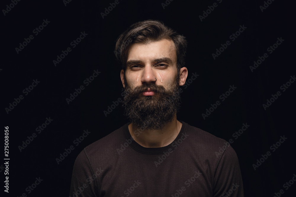 Close up portrait of young man isolated on black studio background. Photoshot of real emotions of male model. Crying, sad, dreary and hopeless. Facial expression, human emotions concept.