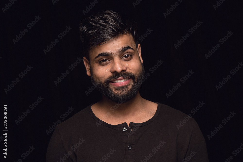 Close up portrait of young man isolated on black studio background. Photoshot of real emotions of male model. Crying throught laughting and smiling. Facial expression, human emotions concept. Close up portrait of young man isolated on black studio background. Photoshot of real emotions of male model. Crying throught laughting and smiling. Facial expression, human emotions concept.