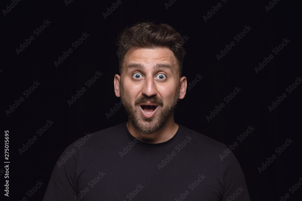 Fototapeta premium Bliska portret młodego człowieka na białym tle na tle czarnego studia. Sfotografowanie prawdziwych emocji modela. Zastanawiający, ekscytujący i zdumiony. Wyraz twarzy, koncepcja ludzkich emocji.