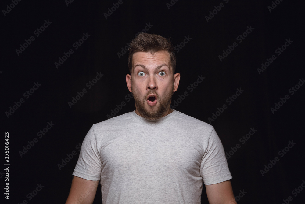 Obraz premium Close up portrait of young man isolated on black studio background. Photoshot of real emotions of male model. Wondering, exciting and astonished. Facial expression, human emotions concept.