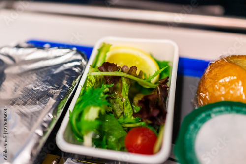 Healthy vegan vegetarian food hot vgml meal on airplane flight with salad vegetables on tray with greens, lemon tomato and bread