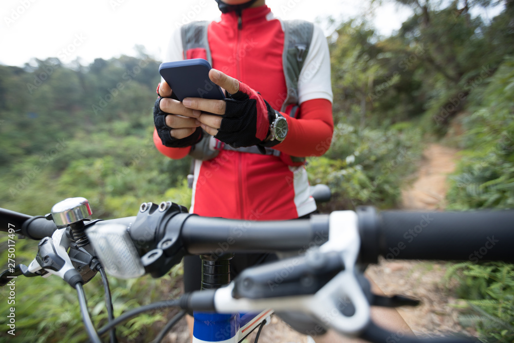 Fototapeta premium Riding on summer hill, holding mobile phone, using online application for searching GPS coordinates while riding bike in forest on sunny day