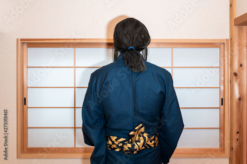 Traditional japanese house with sliding door window with back of man in kimono costume standing with obi sash belt