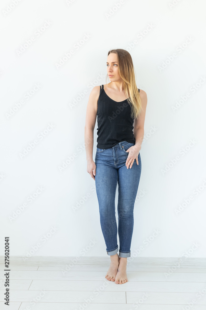 Style and people concept - young woman in jeans standing over the white wall and looks like sexy Style and people concept - young woman in jeans standing over the white wall and looks like sexy