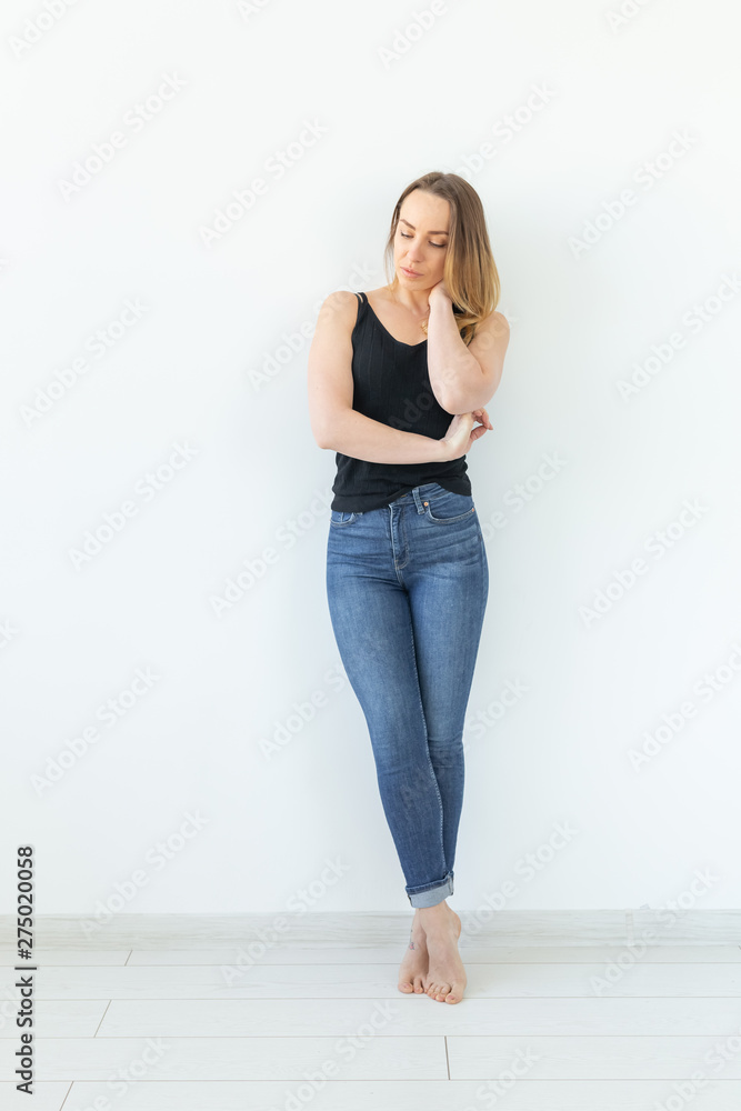 Style and people concept - young woman in jeans standing over the white wall and looks like sexy Style and people concept - young woman in jeans standing over the white wall and looks like sexy