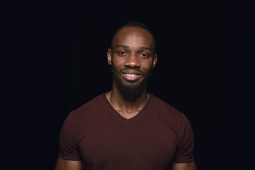 Close up portrait of young man isolated on black studio background. Photoshot of real emotions of male model. Smiling, feeling happy. Facial expression, pure and clear human emotions concept.