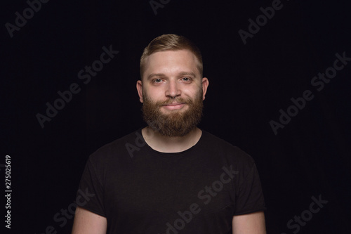 Close up portrait of young man isolated on black studio background. Photoshot of real emotions of male model. Smiling, feeling happy. Facial expression, pure and clear human emotions concept. © master1305