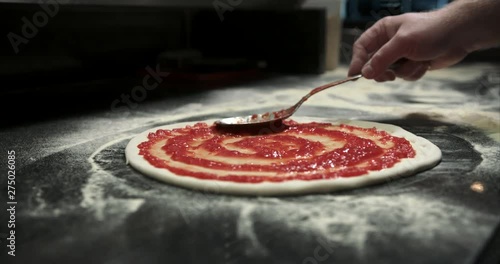 Swirling tomato red sauce on pizza dough. Authentic Neapolitan Pizza cooked in a wood fire oven.