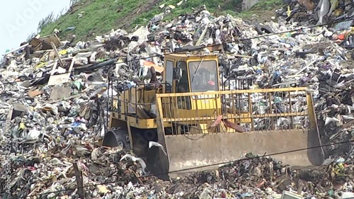 huge tractor with a front end loader and metal wheels is used to move trash in a city dump.  photo